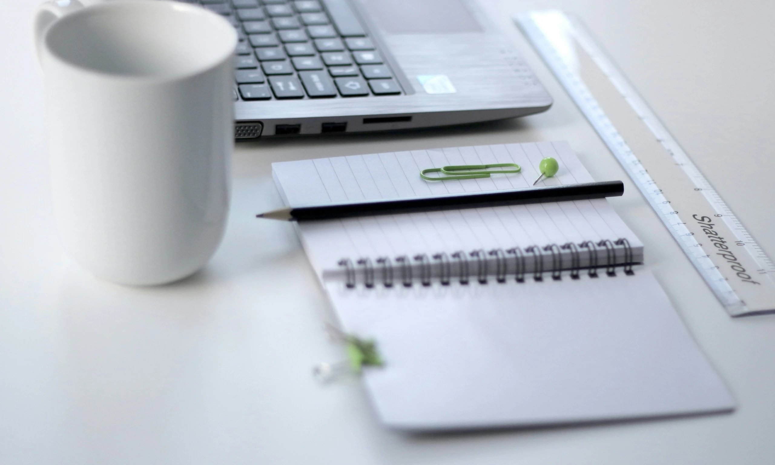 A laptop and a notebook on a desk with a cup of coffee