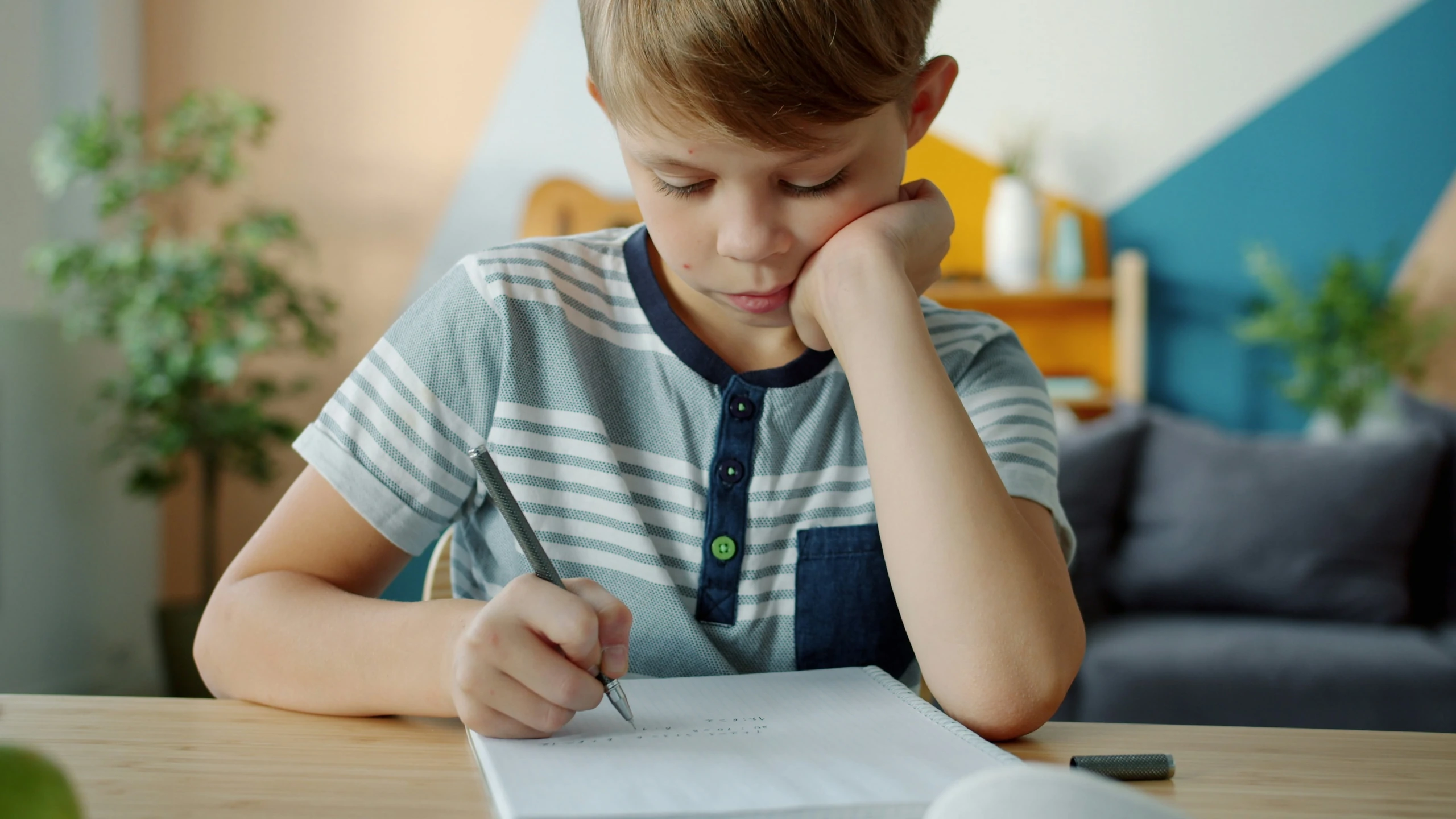 Young student sitting at desk writing in a book and looking worried Young student sitting at desk writing in a book and looking worried